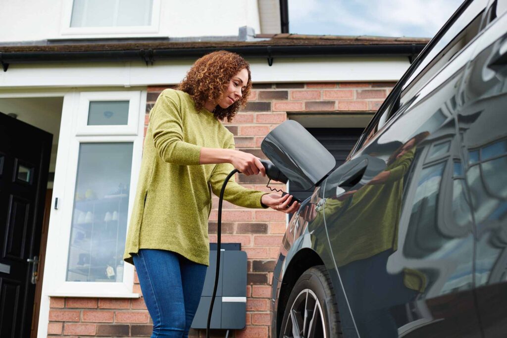 Frau lädt ein Elektrofahrzeug vor ihrem Haus, Nachhaltigkeit durch ReGeTECH Photovoltaik-Technologie.